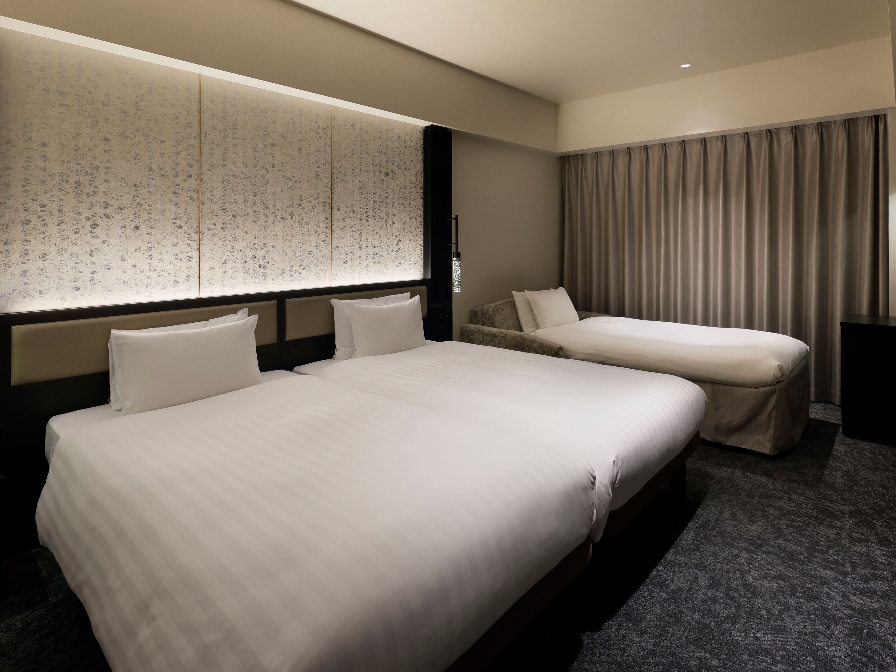 Habitación de hotel con dos camas, un ventanal grande con cortina estampada y alfombra oscura.
