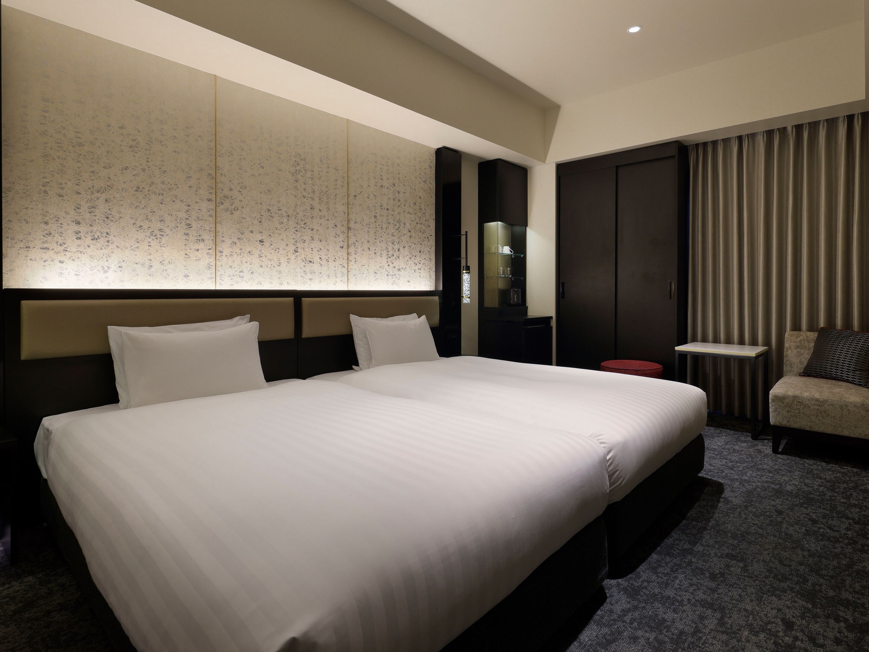 Een hotelkamer met een groot bed, een kleine tafel, een stoel, een kledingkast en een decoratief wandpaneel.