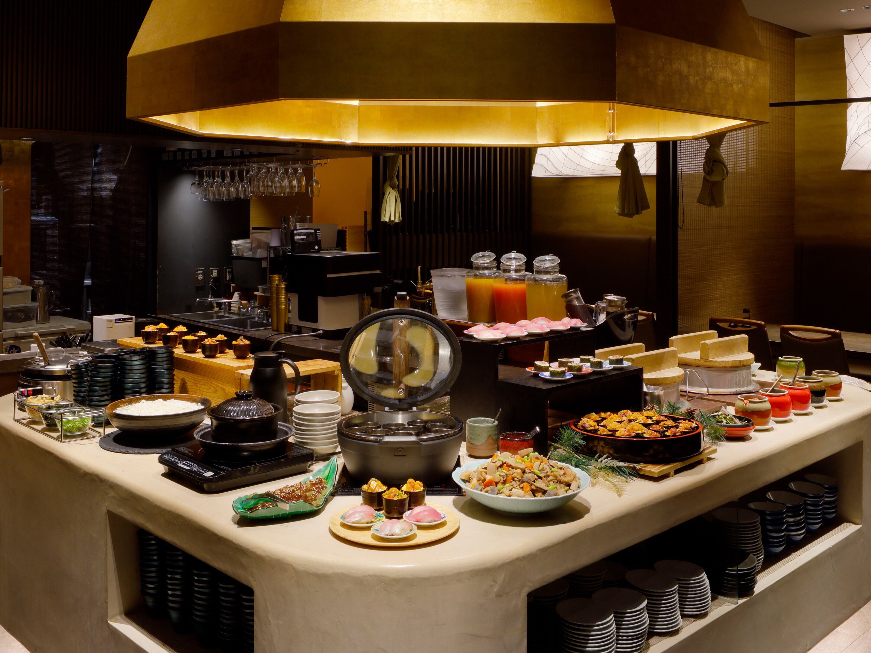 Un buffet proposant une variété de plats et de boissons, une machine à café et un grand luminaire suspendu au plafond.