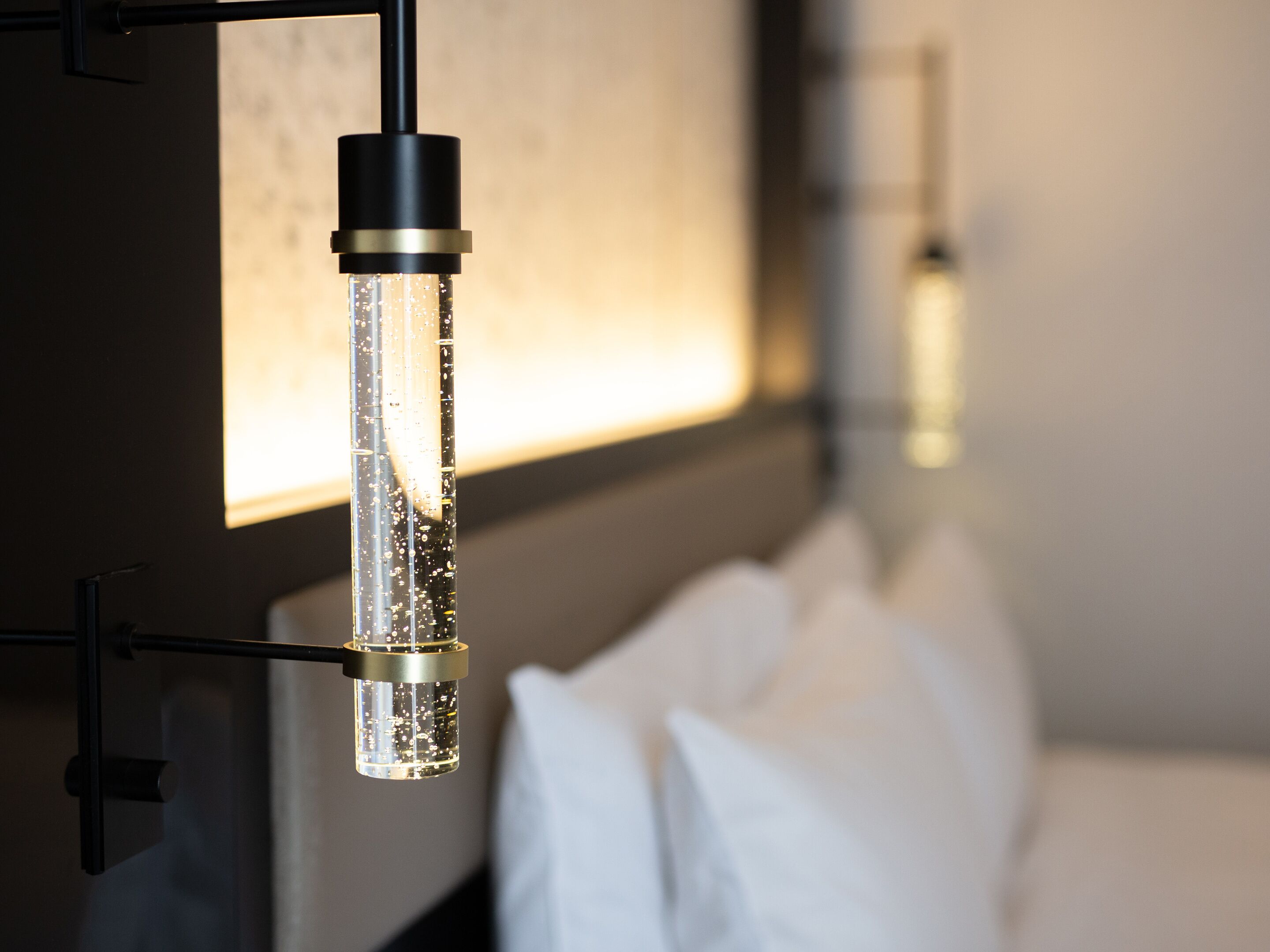 Een moderne kamer met een hanglamp en een bed met witte lakens.