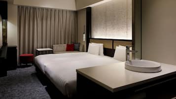 A hotel room with a large bed, a bedside table, a round mirror, and a small red stool.