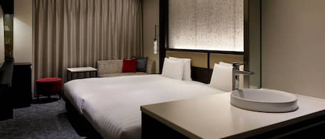 A hotel room with a large bed, a bedside table, a round mirror, and a small red stool.