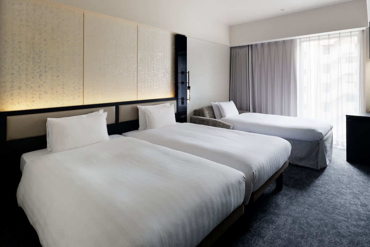 Une chambre d’hôtel avec deux lits, un bureau et une grande fenêtre avec des rideaux.