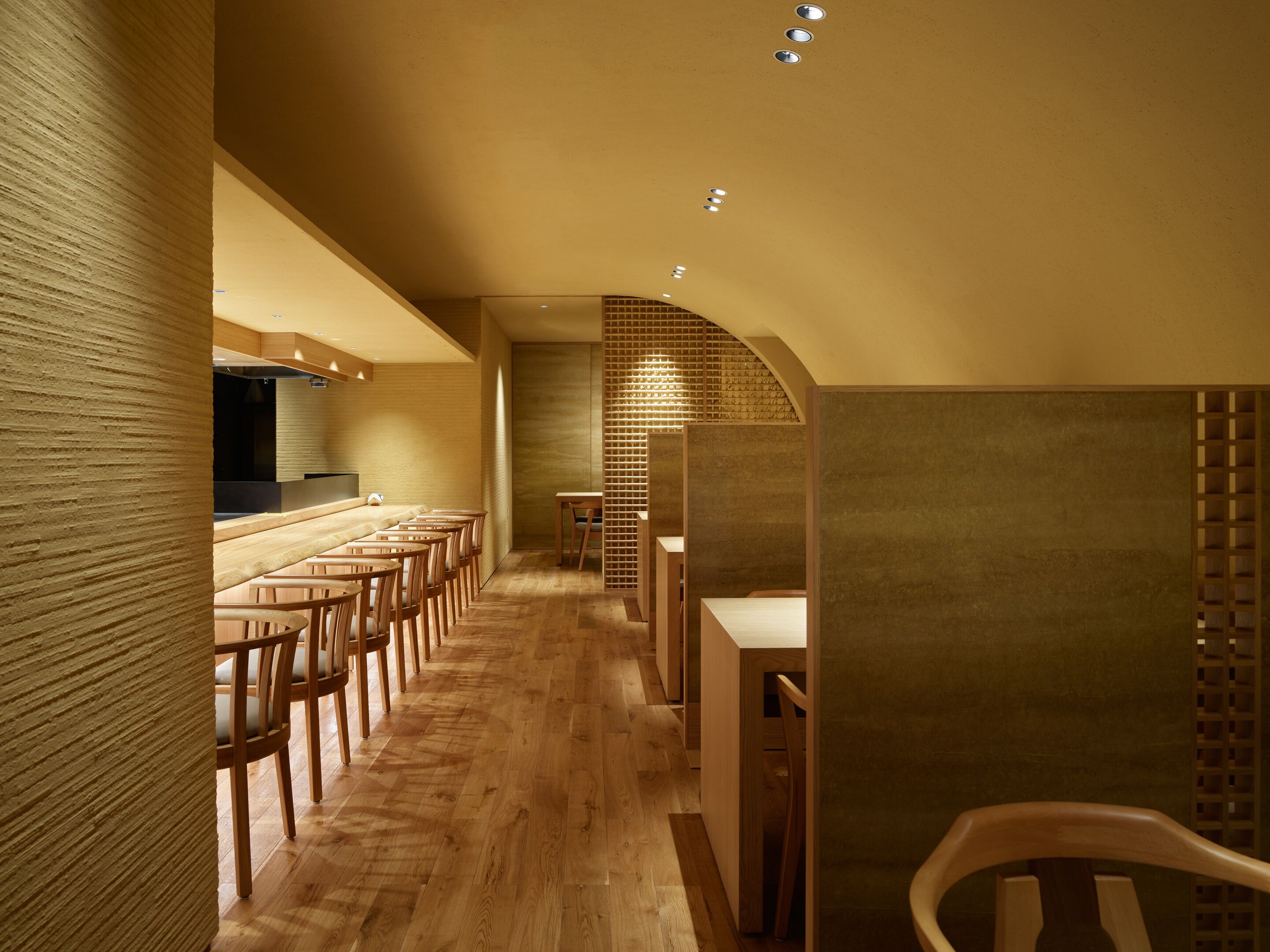 Un interior moderno con suelo de madera, una barra alargada y una zona de asientos con sillas y mesas de madera.