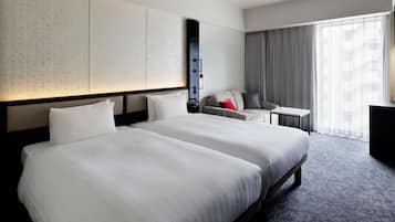 A hotel room with two large beds, a small desk, a sofa, and a large window with curtains.