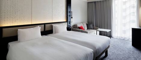 A hotel room with two large beds, a small desk, a sofa, and a large window with curtains.