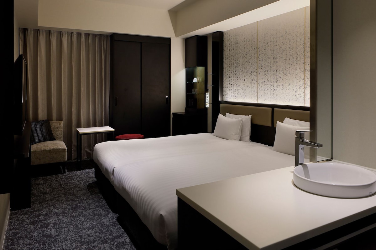 A hotel room with a large bed, a bedside table, a round mirror, and a modern bathroom.