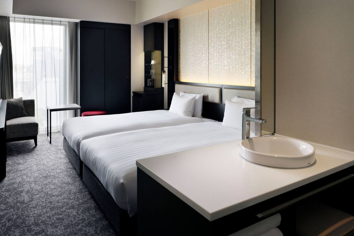 Une chambre d’hôtel avec un grand lit, une table de chevet, une chaise, un bureau et une salle de bain avec un lavabo.