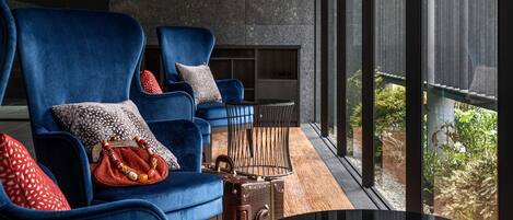 A modern lounge area with blue velvet sofas, a small round table, and a leather suitcase.
