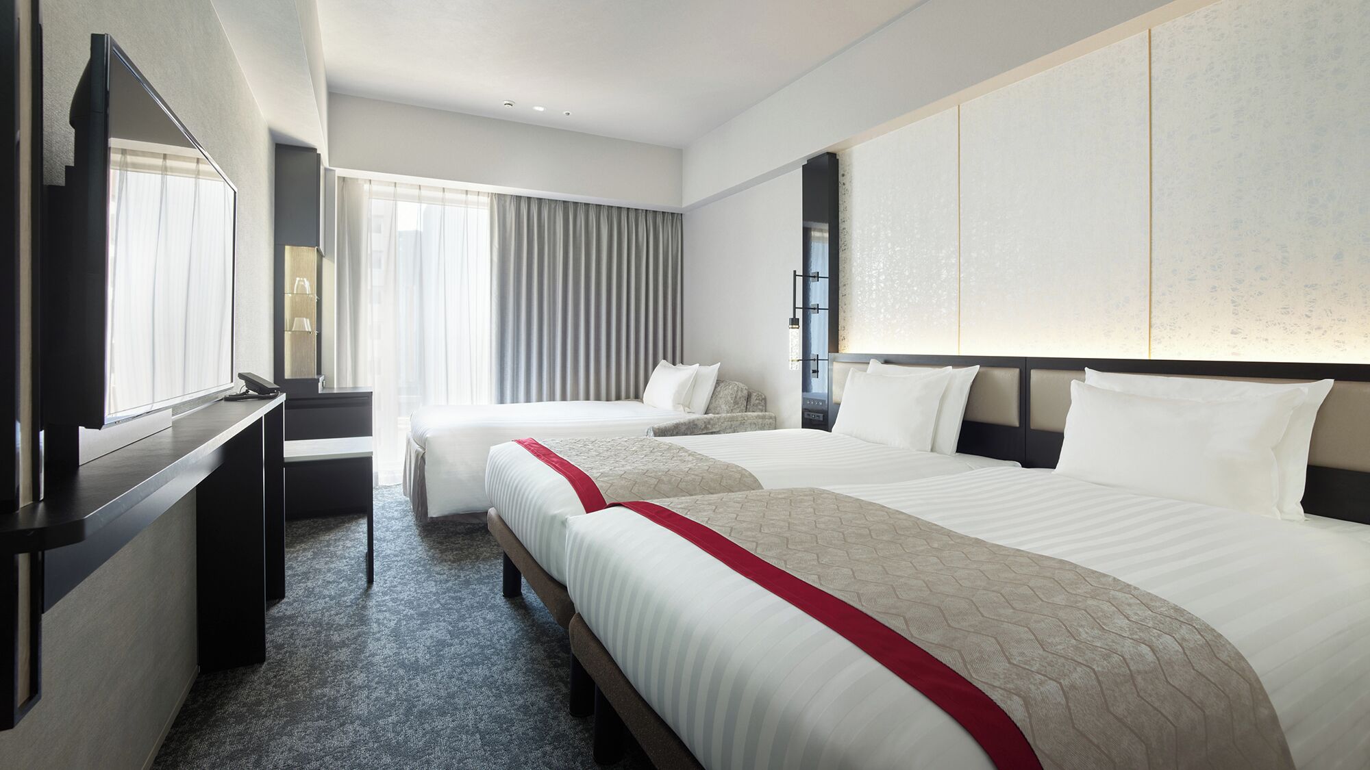 Une chambre d’hôtel avec deux lits, une télévision, un bureau et une grande fenêtre avec des rideaux.