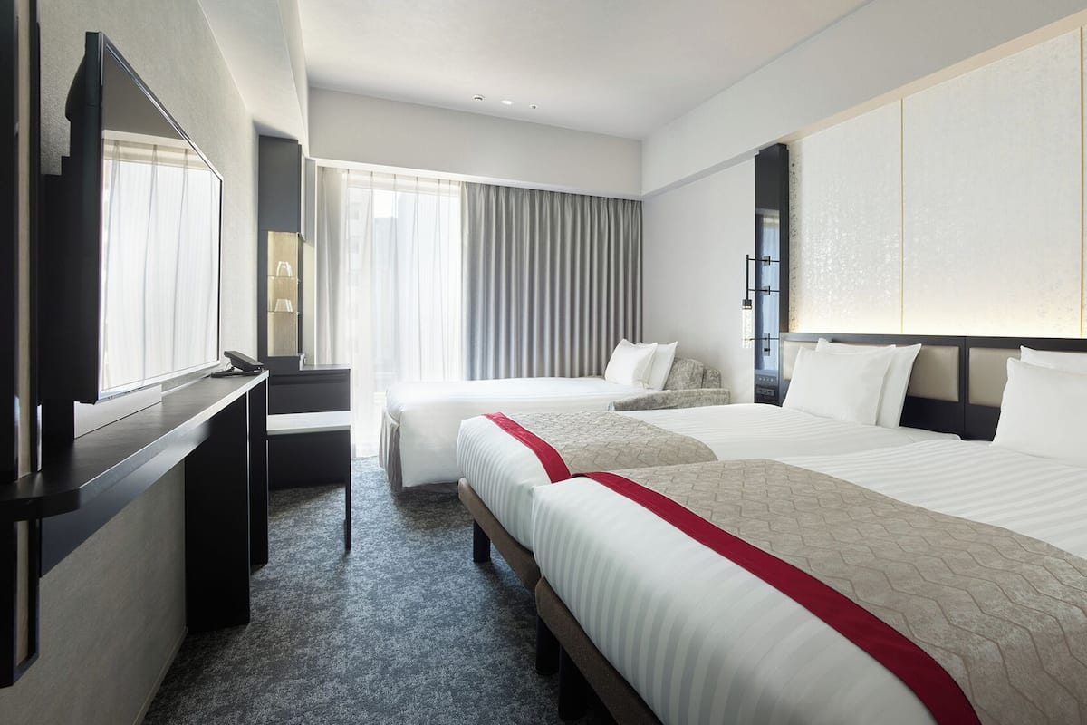 Une chambre d’hôtel avec deux lits, une télévision, un bureau et une grande fenêtre avec des rideaux.