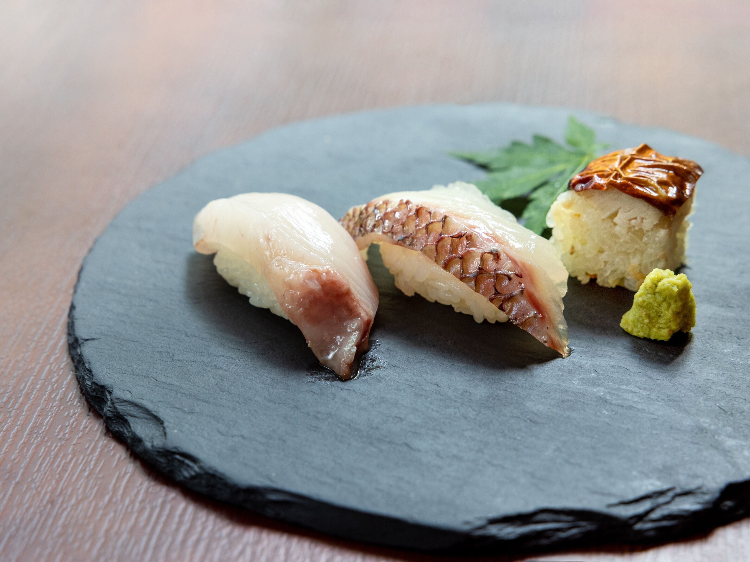 A black slate plate with three pieces of sushi and a small green garnish.