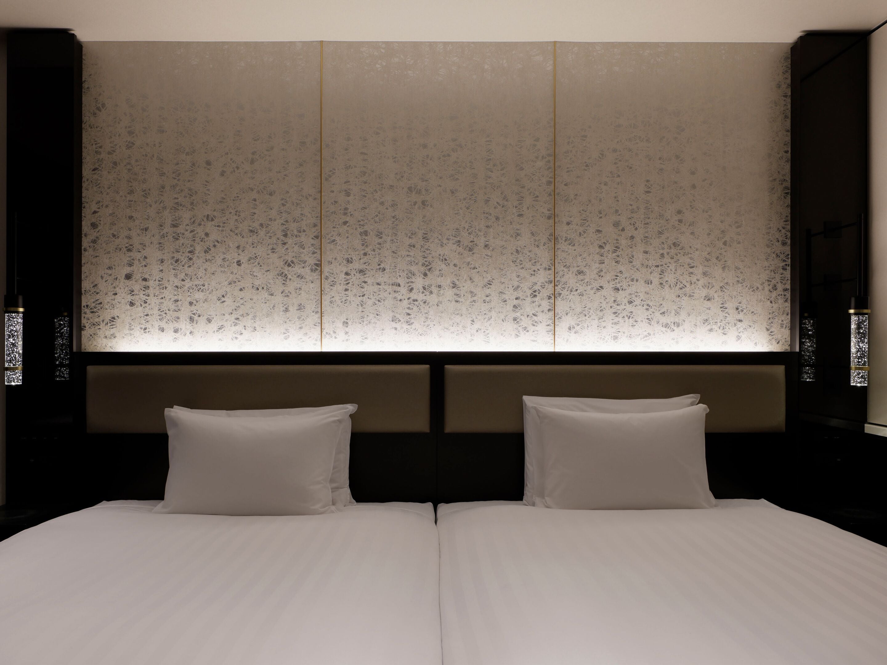 A hotel room with a large bed, two pillows, a headboard with a textured design, and a wall with a patterned design.
