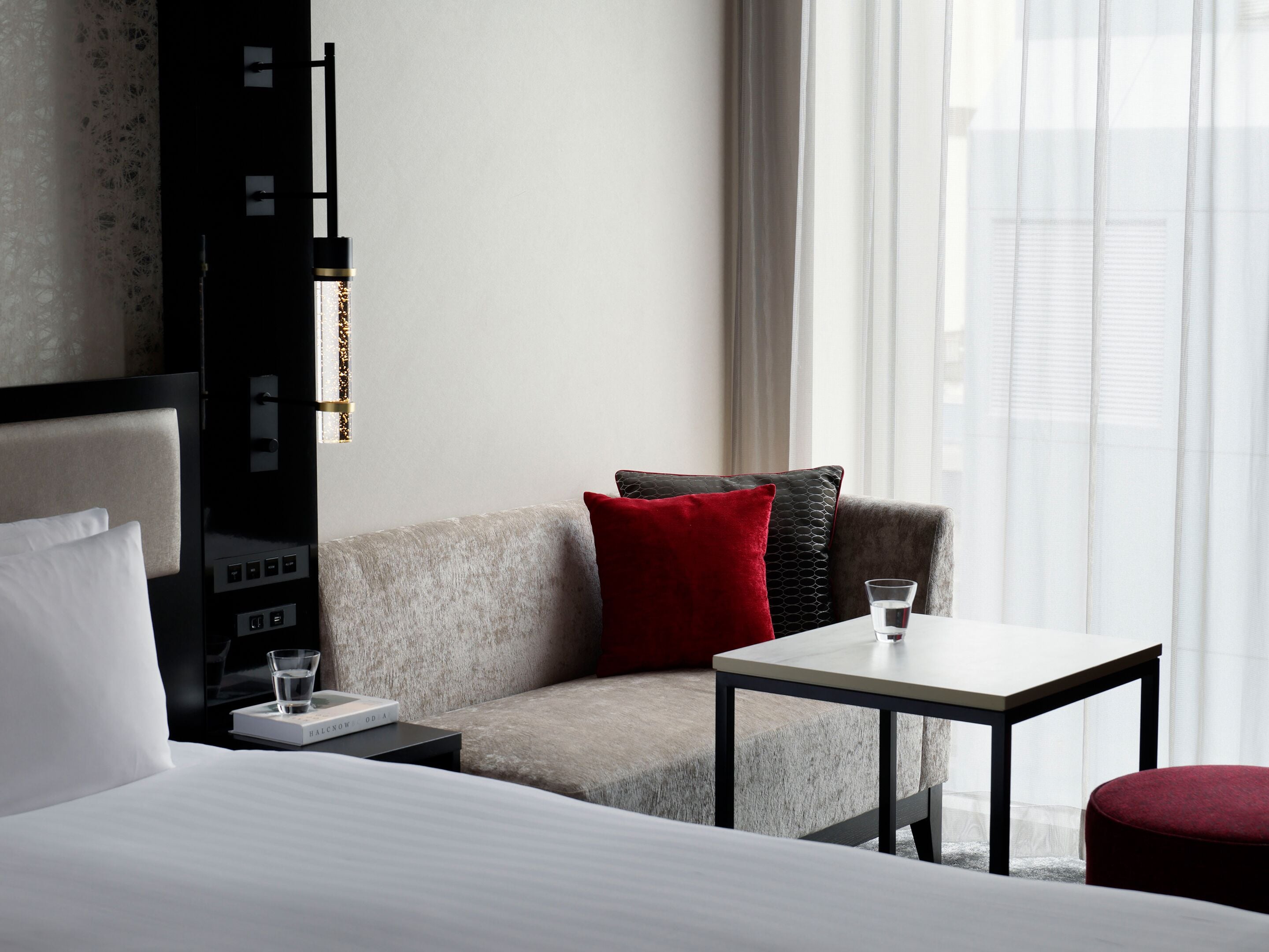 A hotel room with a bed, a sofa, a small table, and a TV stand.
