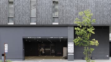 A modern building with a service car entrance, a parking area, and a tree.