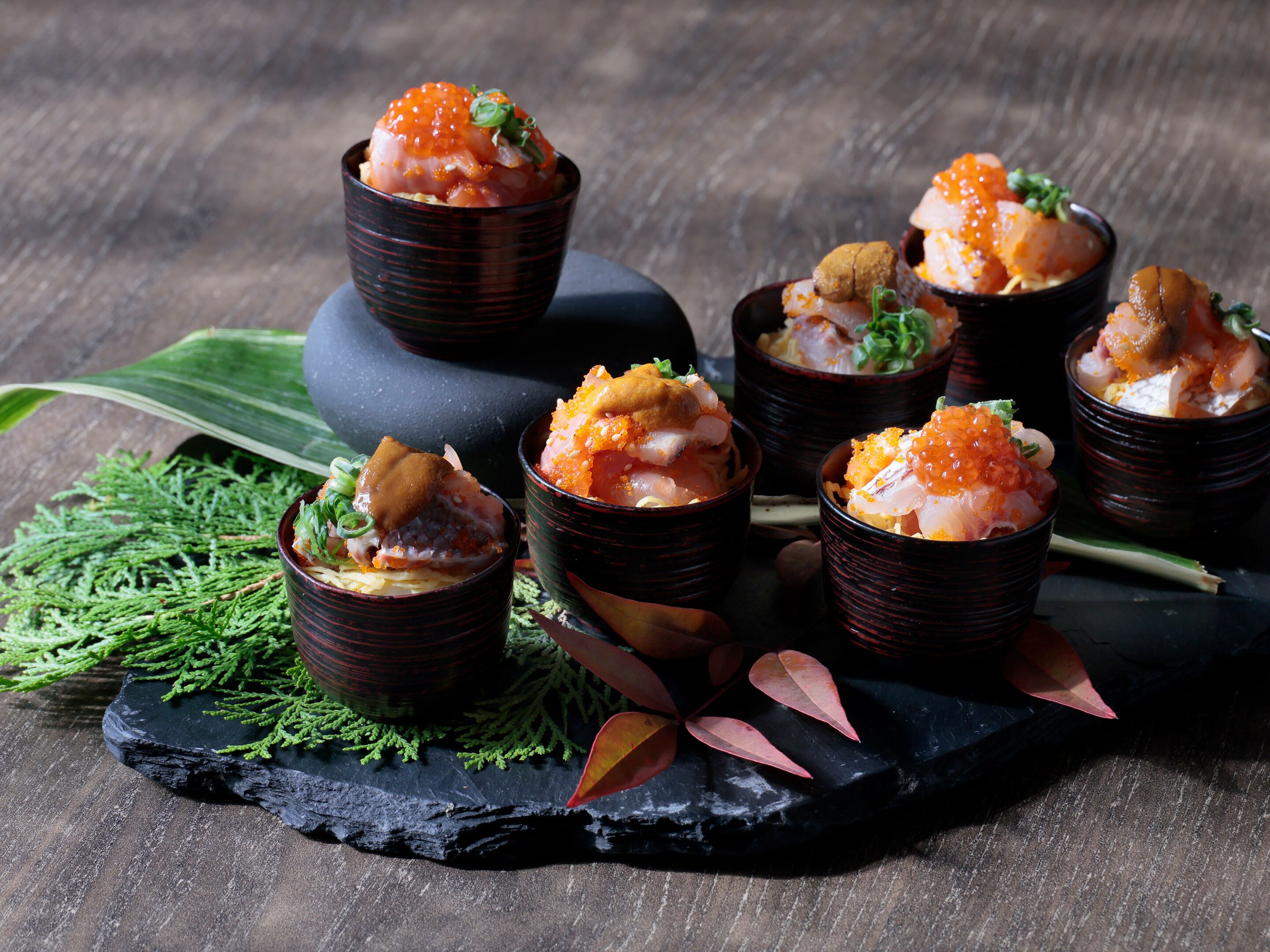 A series of dishes arranged on a dark slate serving board, accompanied by green foliage and decorative leaves.