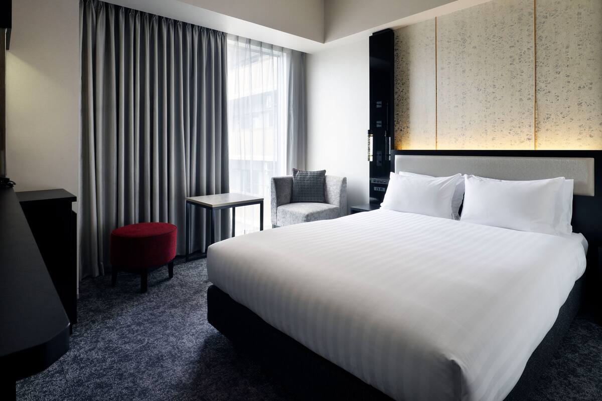 Une chambre d’hôtel avec un grand lit, un bureau, une chaise et un pouf rouge.