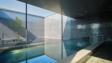 Una piscina interior moderna con paredes de vidrio transparente, suelo de baldosas y diseño minimalista.