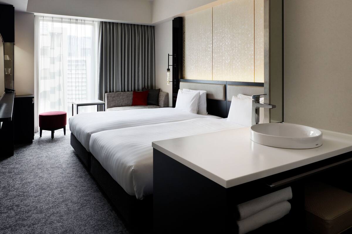Une chambre d’hôtel avec un grand lit, un bureau, une chaise, un miroir rond et une vue sur la ville.
