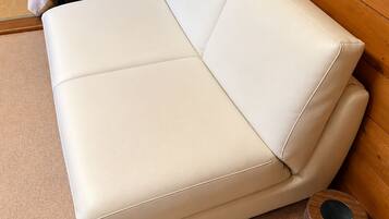 A white leather sofa in a room with wooden walls and a carpeted floor.