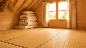 Ein Zimmer mit Tatami-Matten, einem Kissenstapel, einem Fenster mit Vorhängen und einer hängenden Lampenleuchte.