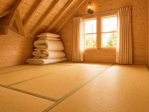 Quarto com esteiras de tatame, uma pilha de almofadas, janela com cortinas e luminária suspensa.