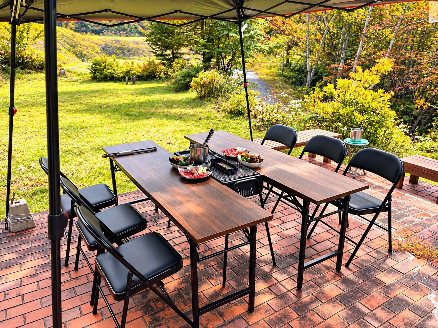 An outdoor patio with a wooden table and chairs, surrounded by a brick floor and greenery.