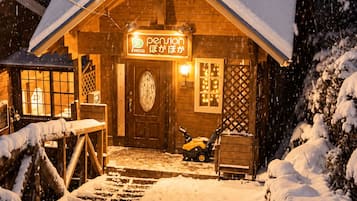 A wooden cabin with a snow-covered roof and a lit sign reading 'pension'.