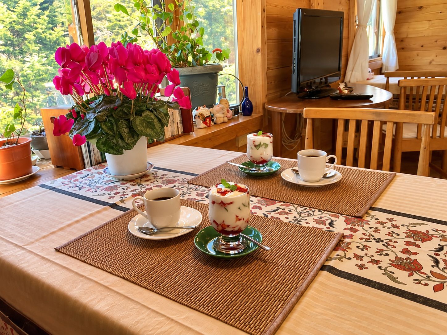 Une pièce chaleureuse avec une table à manger dressée pour deux personnes, un téléviseur et une fenêtre donnant sur un paysage verdoyant.
