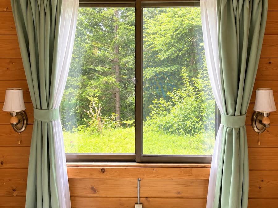 A room with two beds, a window with curtains, and a wall-mounted lamp.