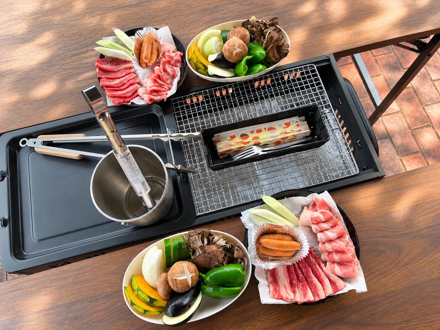 A dining setup with a grill, various meats, vegetables, and a pot on a tray.