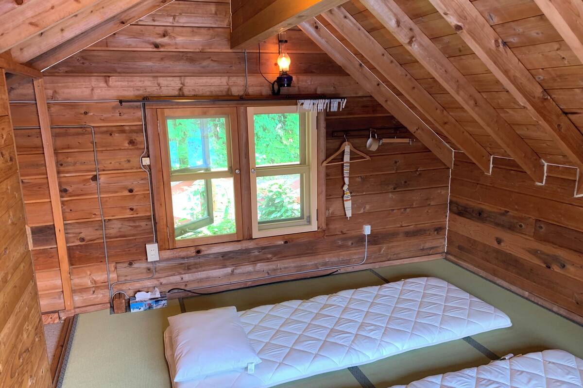 A wooden cabin room with a lofted sleeping area, a window with a view, and a hanging light fixture.
