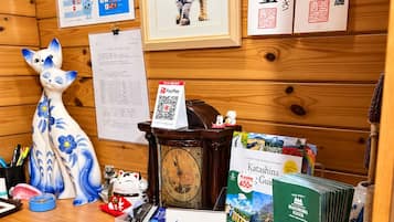 Um balcão de recepção de madeira com um relógio, uma fotografia de um gato emoldurada, uma placa com código QR e folhetos de viagens.