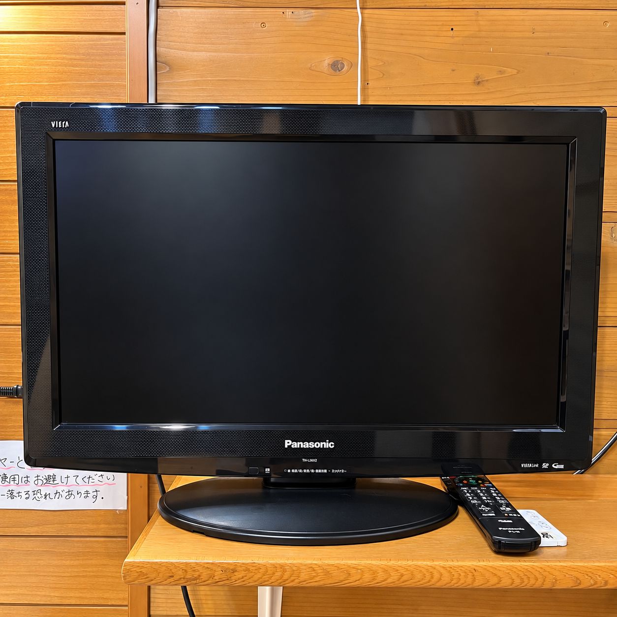Een Panasonic tv op een houten standaard, met een afstandsbediening ernaast.