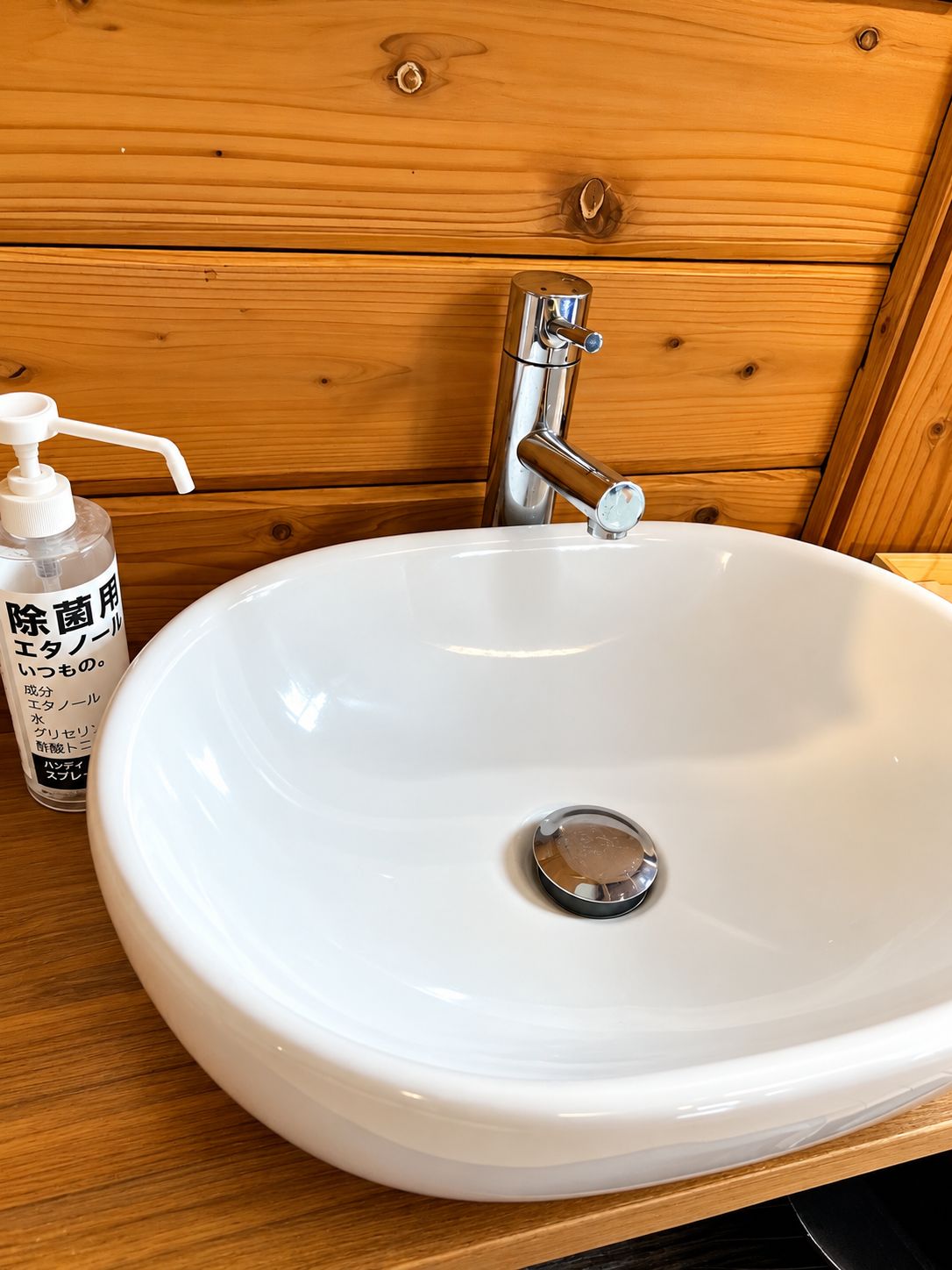 A white ceramic sink with a chrome faucet, a soap dispenser, and a wooden backdrop.
