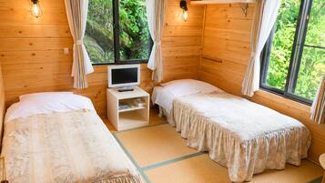 A wooden cabin room with two beds, a television, and a shelf with towels.