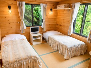 A wooden cabin room with two beds, a television, and a shelf with towels. - Pension Poka Poka (Katashina)