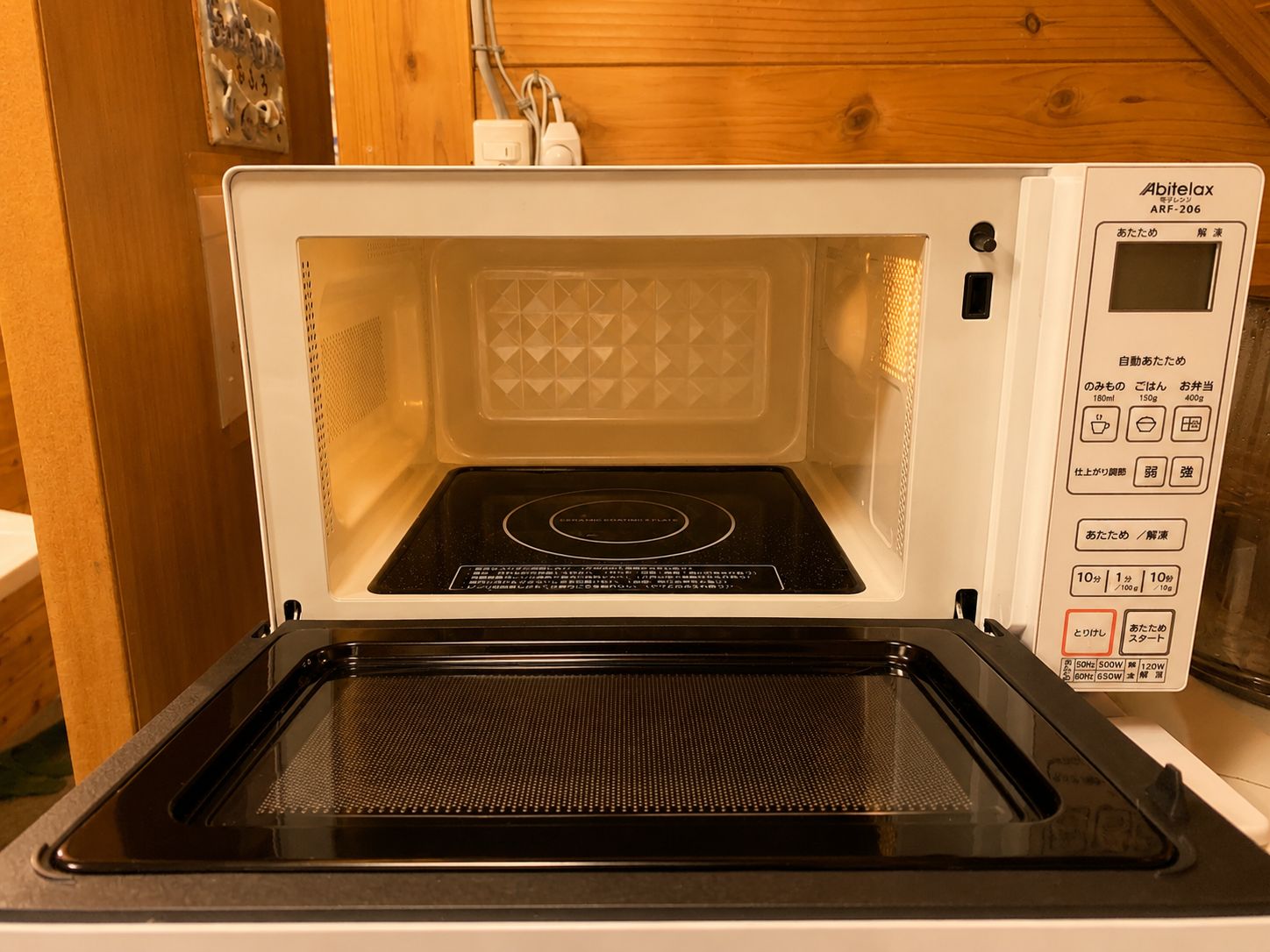 A microwave oven with a digital display and control panel, placed in a kitchen with wooden walls.