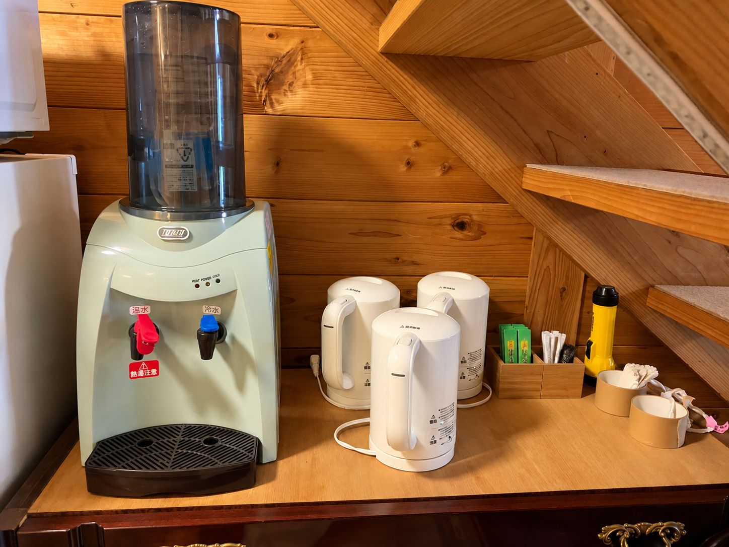 Un sauna équipé d’un panneau de commande, d’un chauffe-eau et de plusieurs appareils de chauffage pour sauna blancs, le tout posé sur une table en bois.