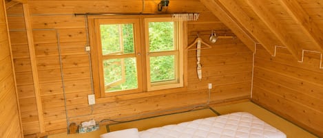 Una habitación de cabaña de madera con una cama, una ventana y una lámpara colgante.