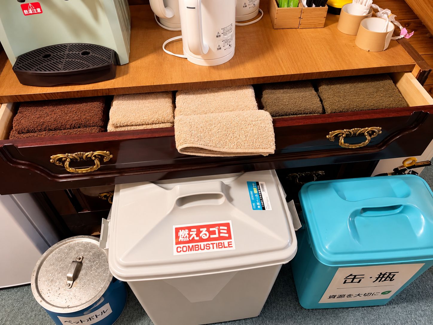 A kitchen counter with a coffee maker, a kettle, and a drawer with various kitchen towels.