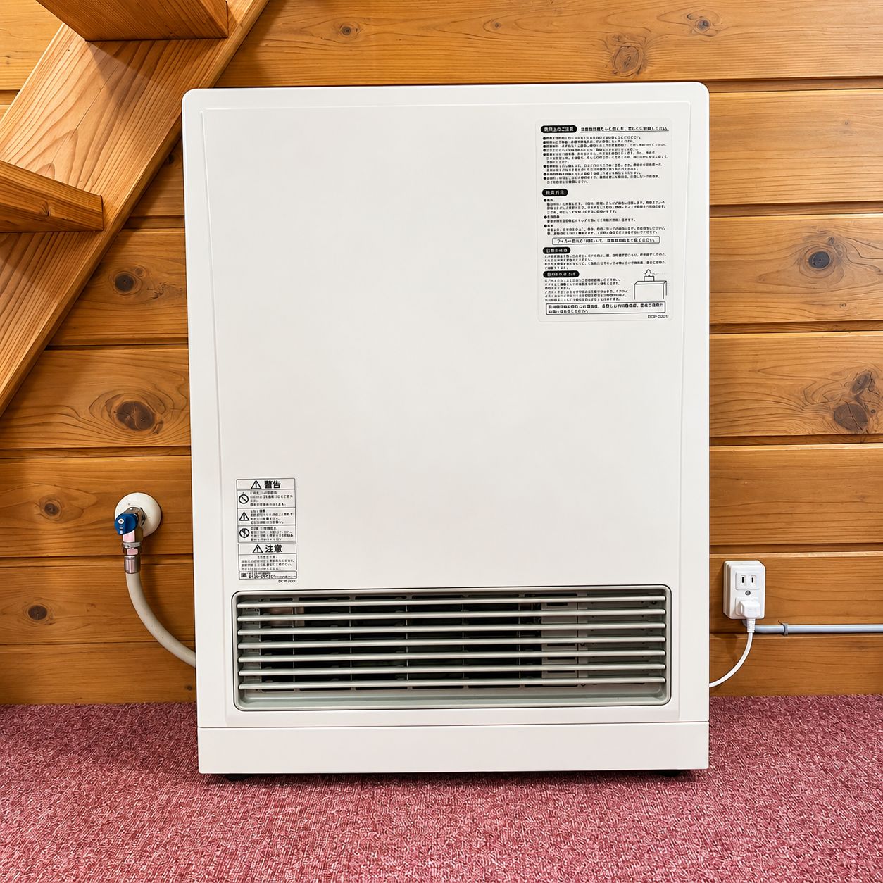 Een witte, verplaatsbare airconditioner tegen een houten wand, met een stopcontact en snoer.