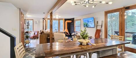 A spacious dining area with a wooden table and benches, a chandelier, and a view of the outdoors through large windows.