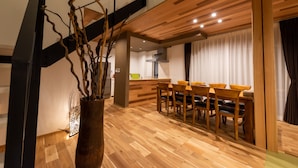 Un interior moderno con una zona de comedor de madera, una escalera y una cocina al fondo.