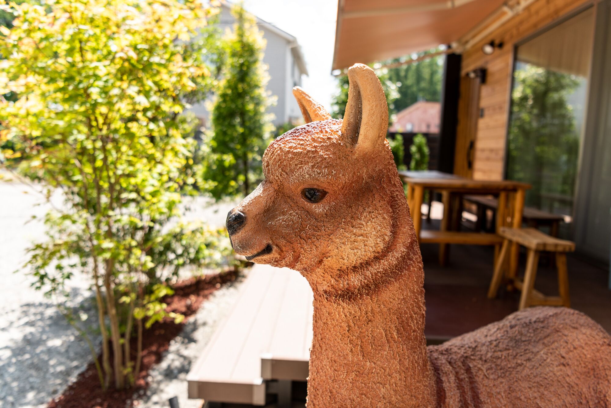 A llama sculpture outdoors, with a wooden table and chairs in the background.