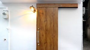 A wooden door with a sliding mechanism, a light fixture above it, and a white wall with a small electrical box to the left. - Samy's Guest House (Osaka)