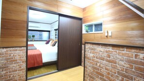 A hotel room with a sliding door leading to a bed, a small window with a plant, and a brick wall design. - Samy's Guest House (Osaka)