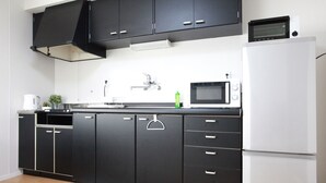 A modern kitchen with black cabinets, a white refrigerator, a microwave, and a sink. - Samy's Guest House (Osaka)