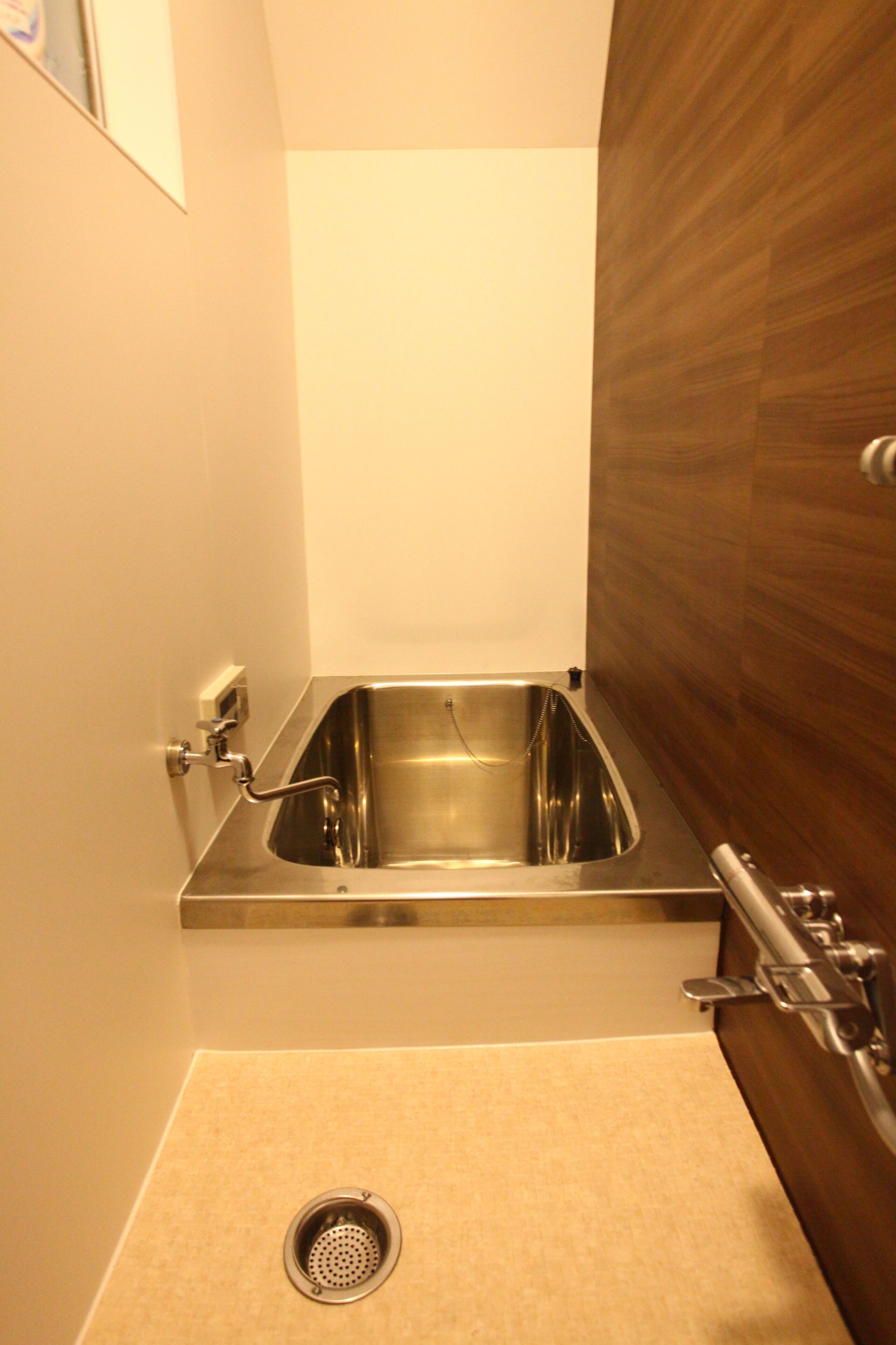 A small bathroom with a stainless steel sink, a wooden vanity, and a beige floor.