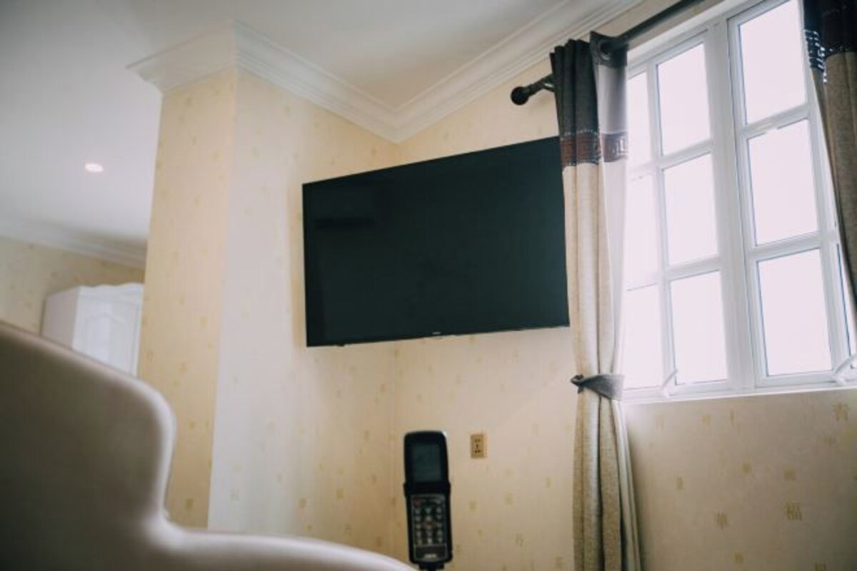 A room with a mounted television, a window with curtains, and a wall-mounted telephone.